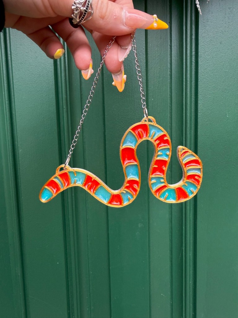 a blue and red gummy worm shaped ornament suspended by a chain