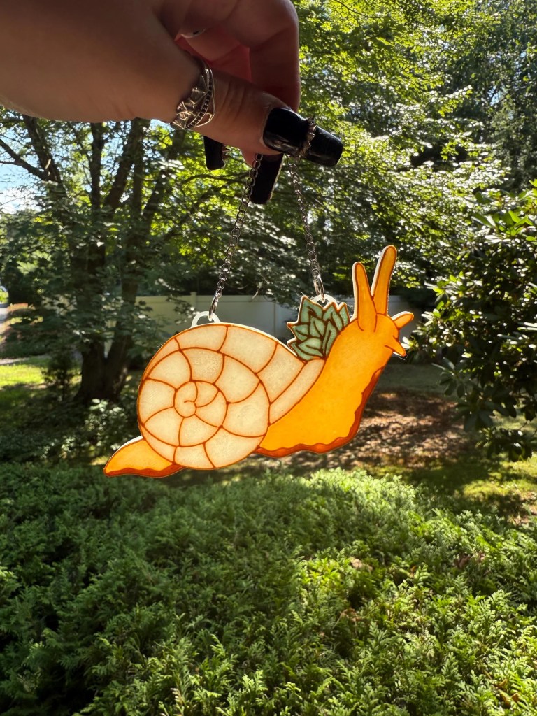 A snail-shaped ornament with an orange body, white shell and leafy detail on its back.